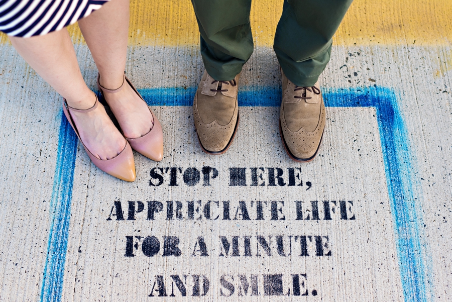 An engaged couple stand on a sign telling you to appreciate life.